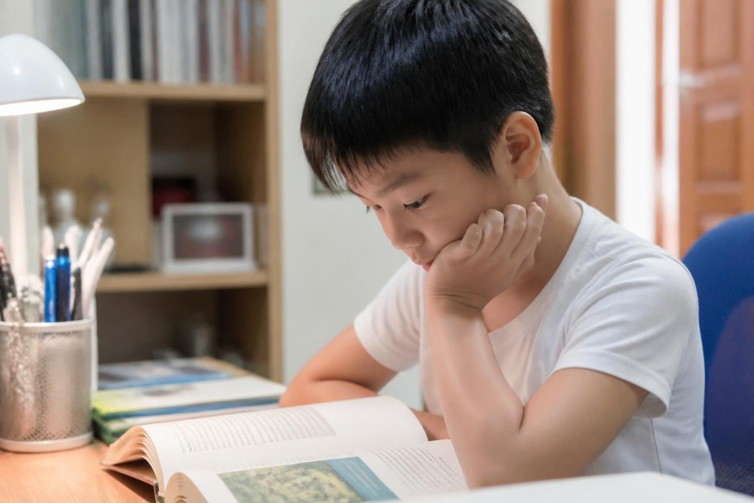 Bé trai chống cằm tì má khi ngồi học bài - Nha khoa Bác sĩ Trung Long Biên