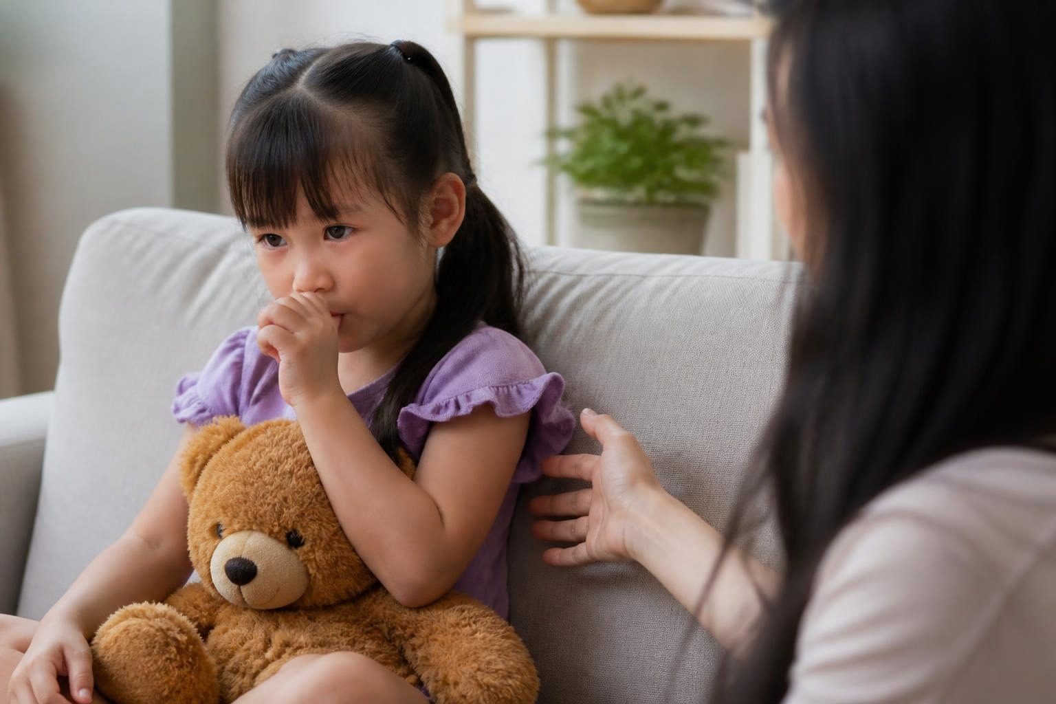 Bé gái ôm gấu bông mút tay, mẹ ngồi cạnh nhắc nhở - ảnh minh hoạ thói quen mút tay là nguyên nhân gây khớp cắn hở