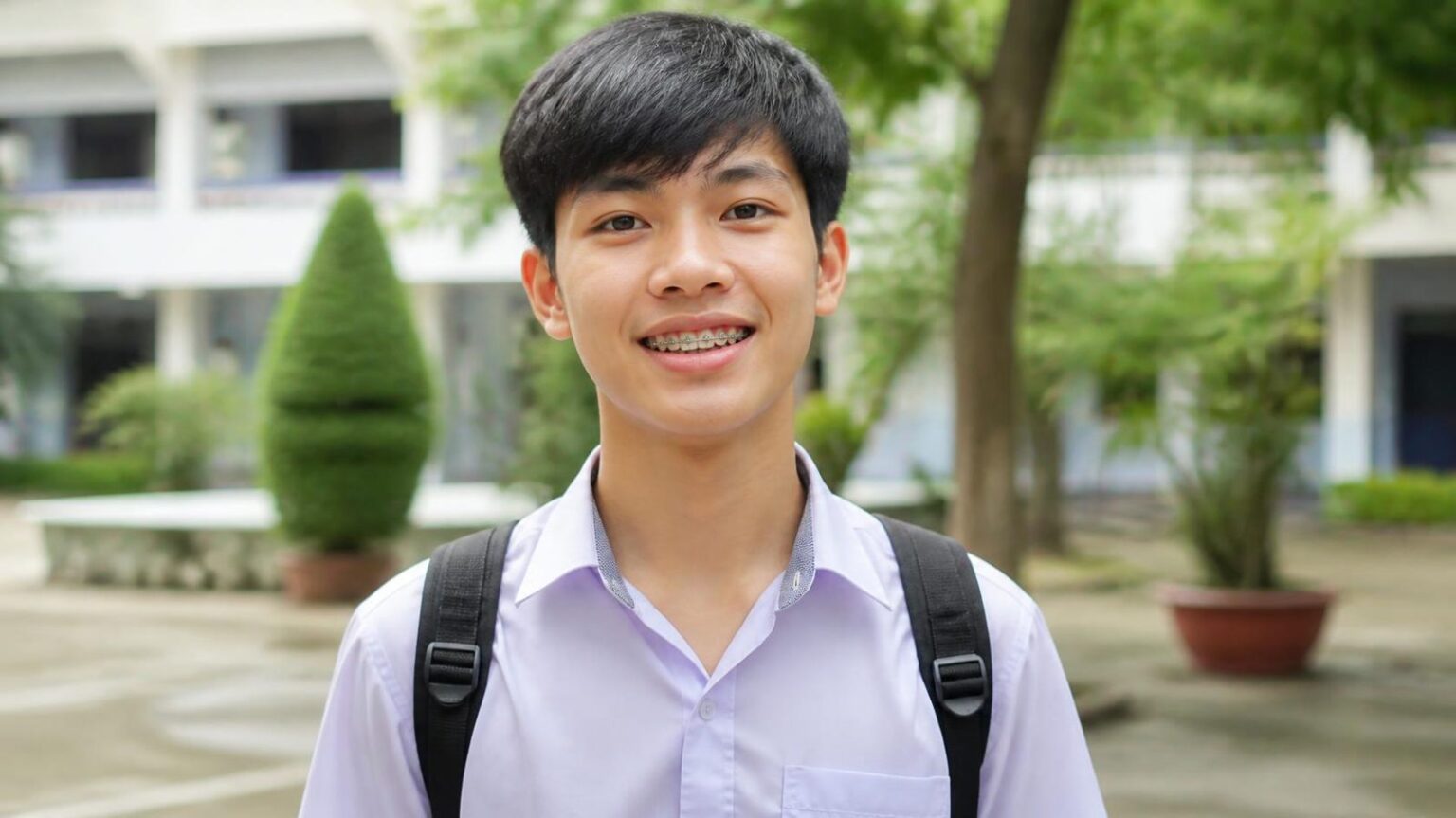 Nam sinh đeo niềng răng mắc cài mỉm cười ở sân trường, các vấn đề thường gặp khi đeo mắc cài - ảnh minh hoạ Nha khoa Bác sĩ Trung Long Biên