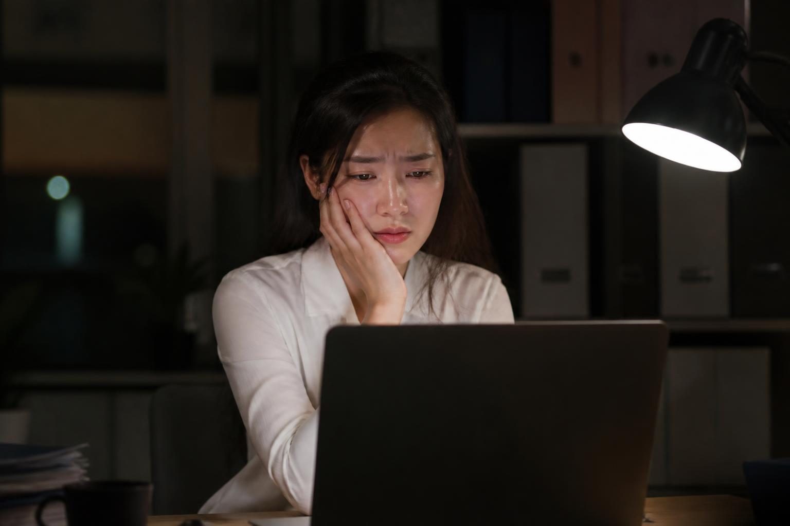 Nhân viên văn phòng căng thẳng làm việc khuya, tay xoa hàm, căng thẳng là một nguyên nhân gây nghiến răng - ảnh minh hoạ