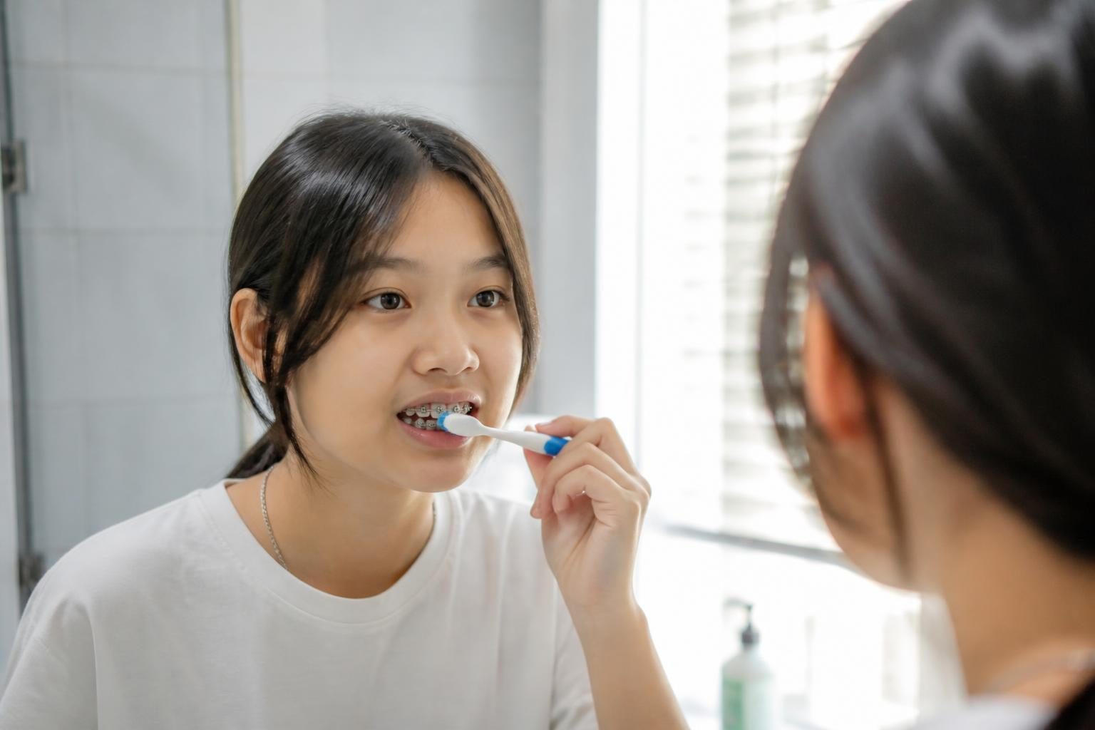 Cô gái đang niềng răng chải răng kỹ trước gương mỗi sáng, thói quen tốt để niềng răng hiệu quả - ảnh minh hoạ