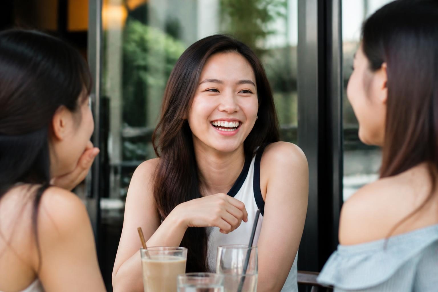 Cô gái cười tự tin bên bạn bè ở quán cà phê với hàm răng đều sau niềng răng - ảnh minh hoạ