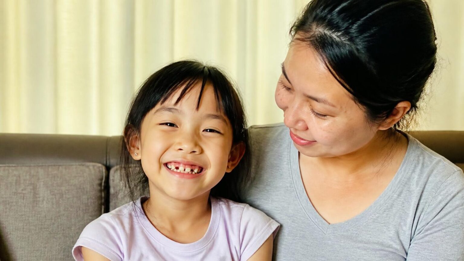 Bé gái 7 tuổi đang thay răng ngồi cười cùng mẹ ở nhà, tuổi nên khám chỉnh nha lần đầu cho trẻ - ảnh minh hoạ Nha khoa Bác sĩ Trung Long Biên