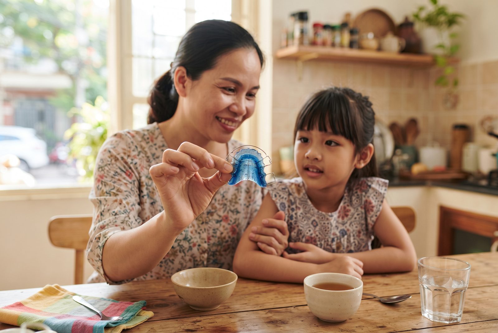 Mẹ cầm khí cụ chỉnh nha tháo lắp cho bé gái xem tại bàn bếp - ảnh minh hoạ khí cụ chỉnh nha trẻ em