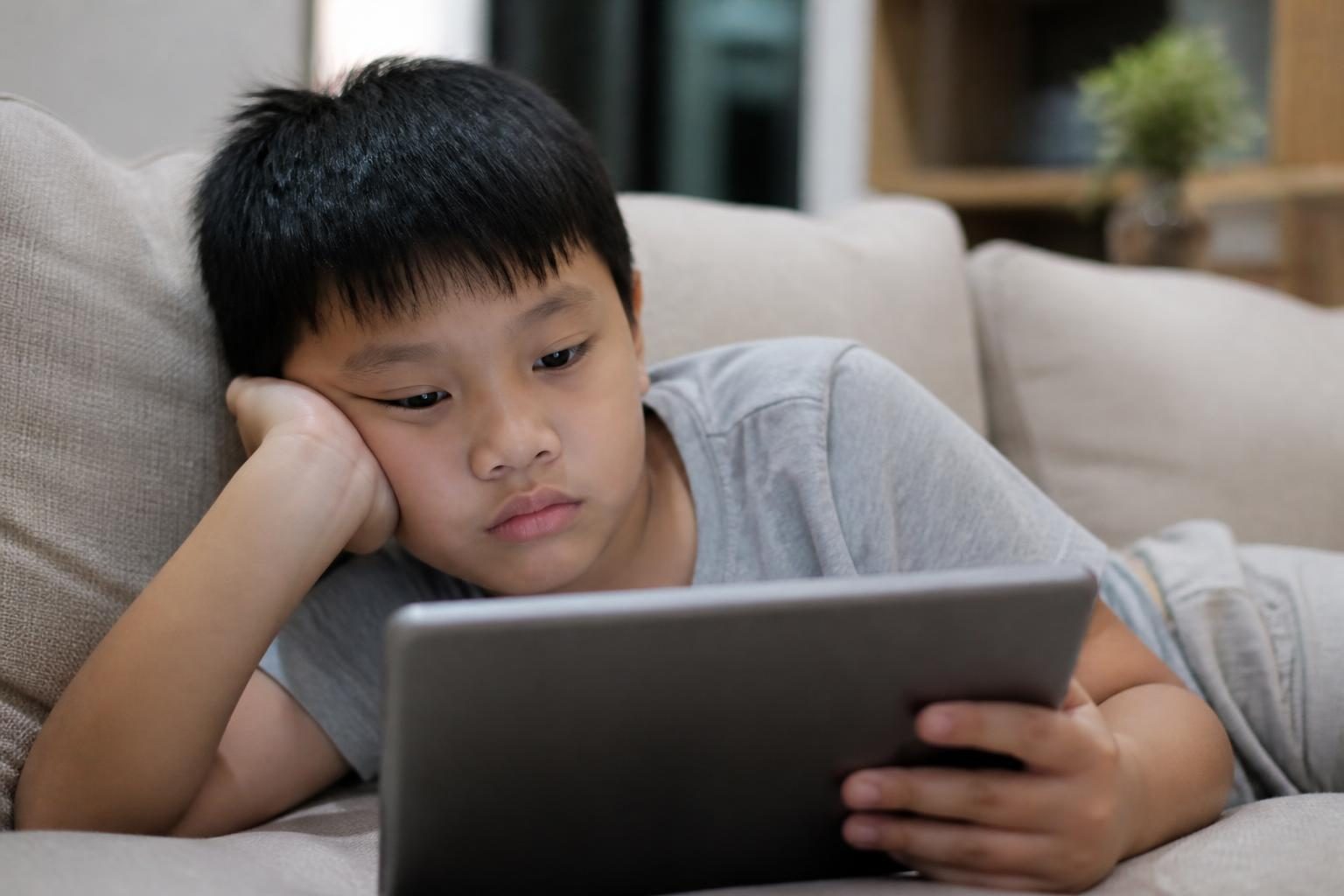 Bé trai nằm tì má lên tay khi xem máy tính bảng, thói quen có thể góp phần gây khớp cắn chéo - ảnh minh hoạ