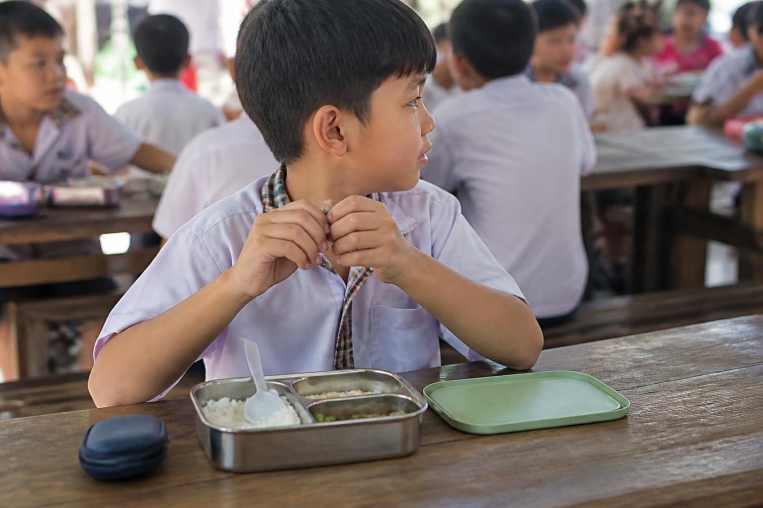 Cậu bé ăn trưa ở trường, hộp đựng máng trong suốt để bên cạnh, trẻ dễ quên đeo đủ giờ - ảnh minh hoạ giới hạn máng trong suốt ở trẻ em