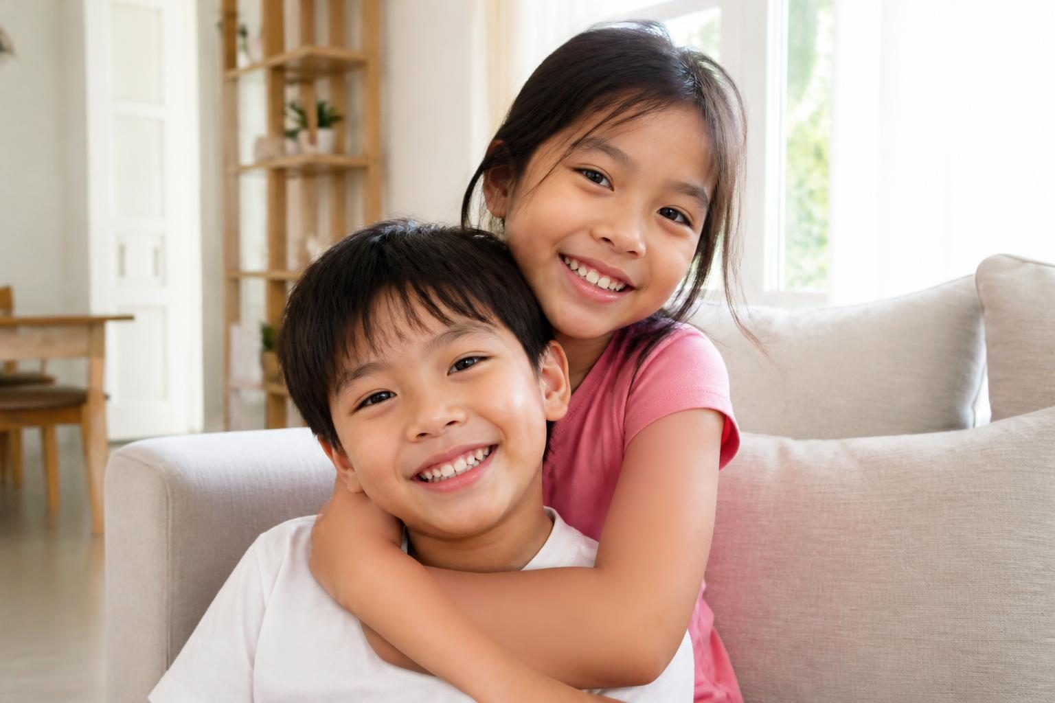Hai chị em nhỏ tuổi cười tươi ở phòng khách, trẻ trong độ tuổi thay răng là đối tượng nên trám bít hố rãnh - ảnh minh hoạ